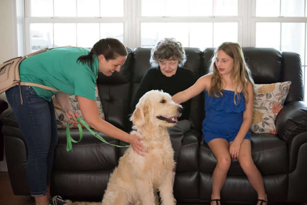 A woman is petting a dog as two girls relax on a couch