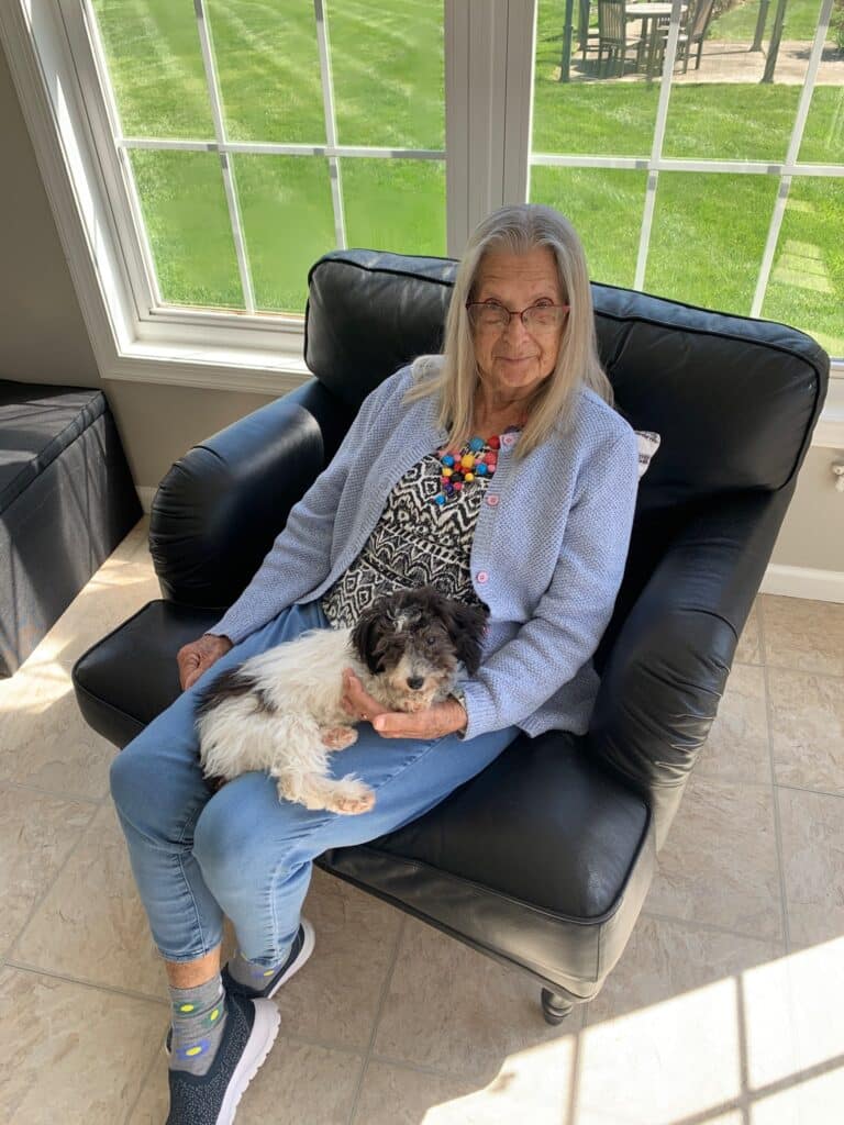 A senior woman seated on a black chair with her dog