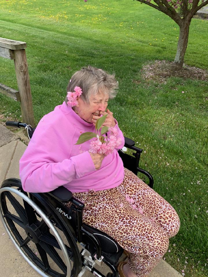 An elderly woman in a wheelchair enjoys a flower