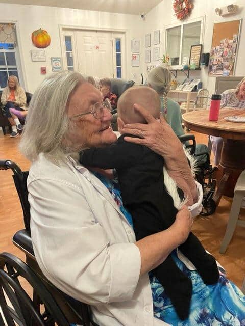 An elderly woman in a wheelchair embraces a baby